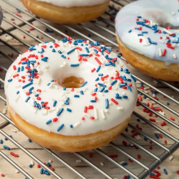 White and blue frosted donuts with red, white, and blue sprinkles on a cooling rack.