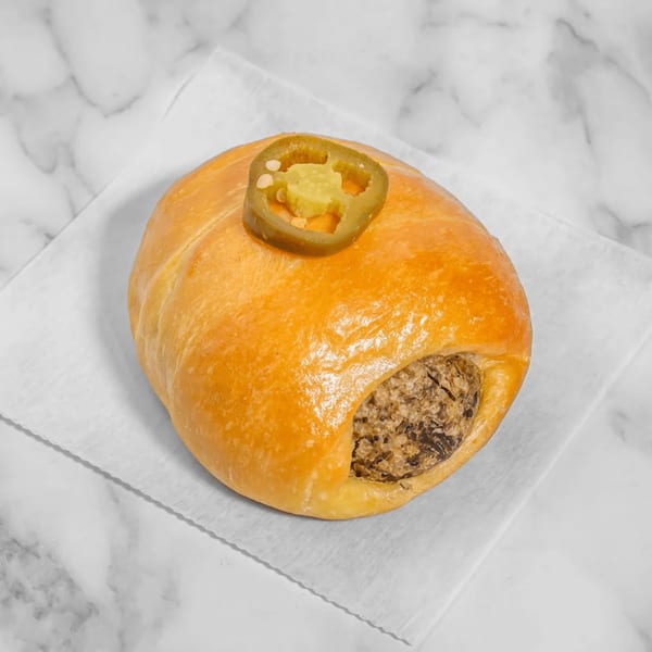A golden-brown kolache with a savory filling and a sliced jalapeño on top, on a white napkin.