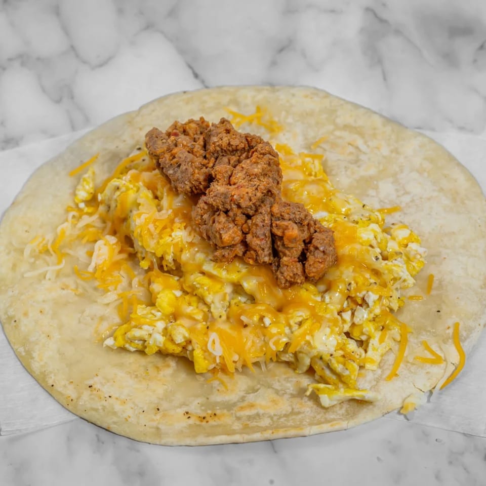 A flour tortilla filled with scrambled eggs, shredded cheese, and chorizo on a white marble surface.