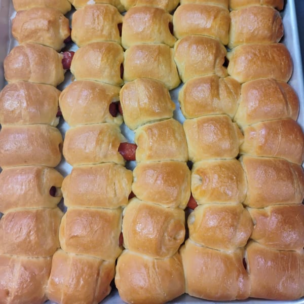 Rows of golden-brown pigs in a blanket, with hot dogs peeking out, on a baking sheet.