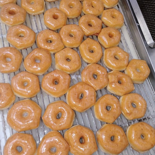Freshly glazed Krispy Kreme donuts on a cooling rack, with some still dripping glaze.