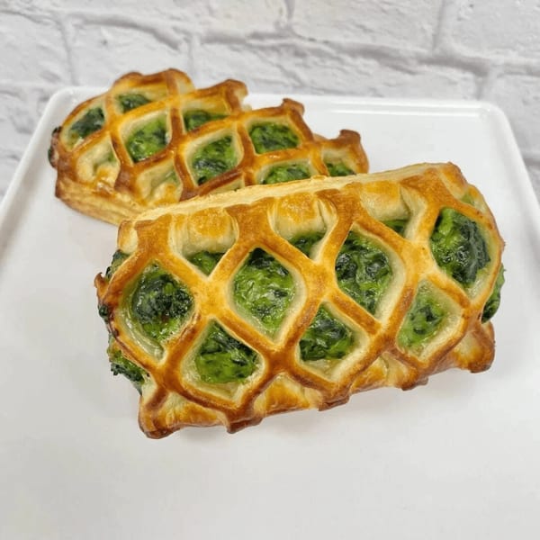 Two golden-brown lattice pastries filled with vibrant green spinach, presented on a white rectangular plate.