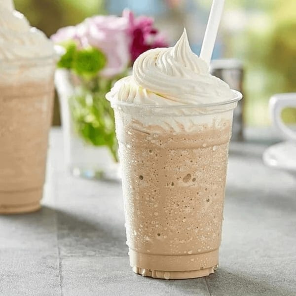 Iced coffee drink with whipped cream and a straw, with flowers in the background.