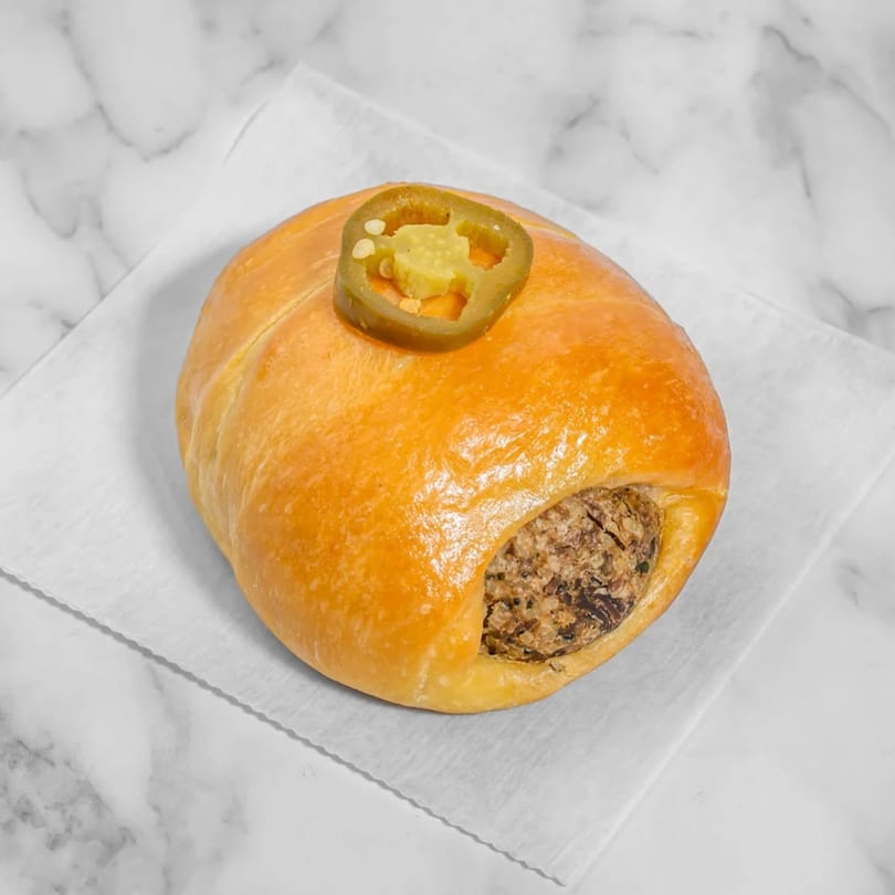 A golden-brown kolache with a savory filling, topped with a sliced jalapeño, on a white napkin.