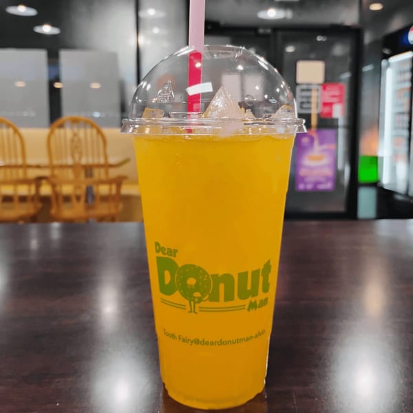 A yellow drink with ice and a pink straw in a "Dear Donut Man" branded cup on a table.