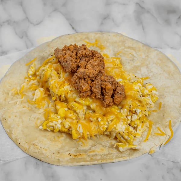 A breakfast burrito with scrambled eggs, shredded cheese, and chorizo on a marble surface.