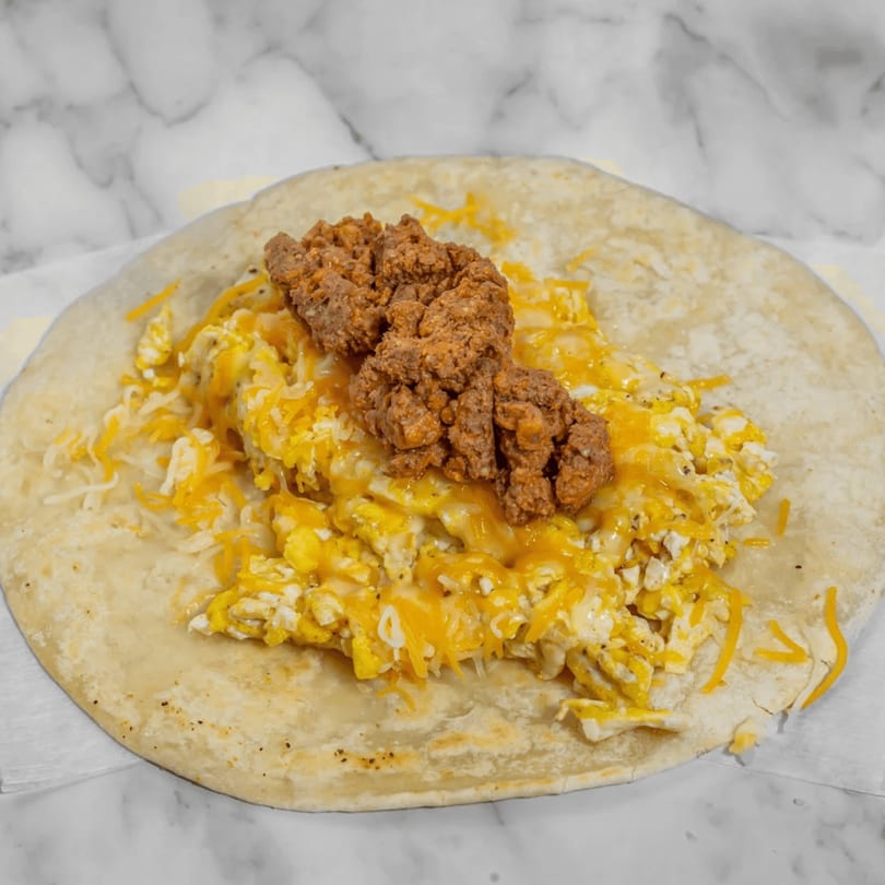 A breakfast burrito with scrambled eggs, shredded cheese, and chorizo on a marble surface.